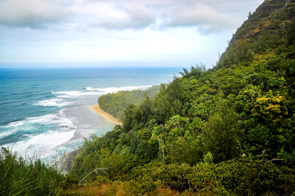 mujer caminando rumbo a napali coast por sendero angosto con caida al mar